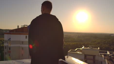 A-man-with-a-laptop-walks-on-the-roof-at-sunset-and-looks-at-the-city-from-a-height-at-sunset.